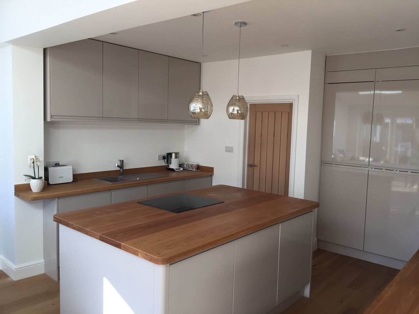 Handleless grey gloss kitchen with oak-topped island